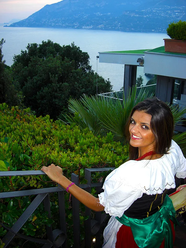 A dancer in costume with a lace blouse leaning on the railing, the bay behind her