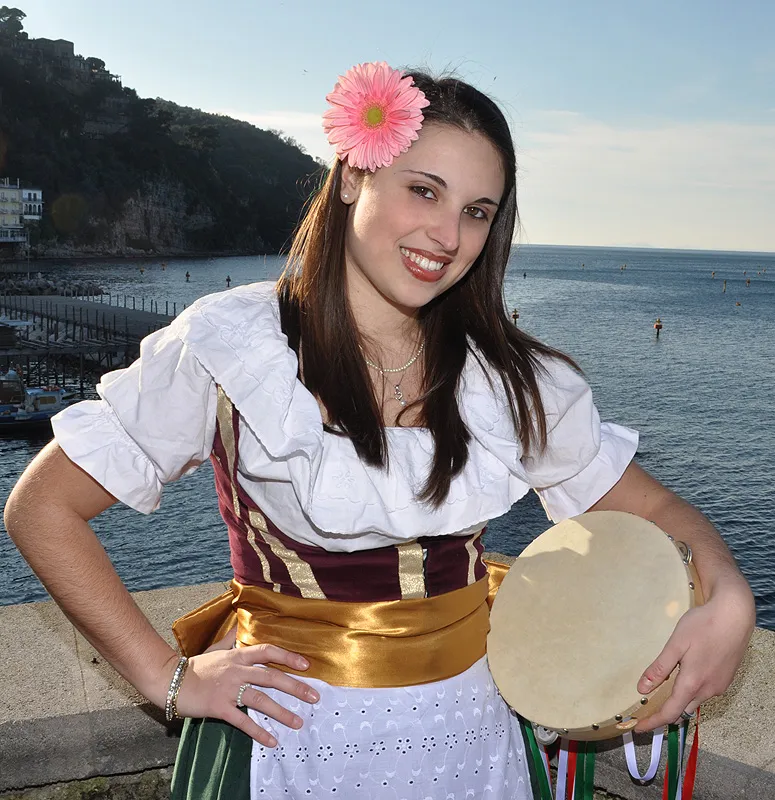 A dancer with a pink flower in her hair and a tambourine, Sorrento’s harbour in the background