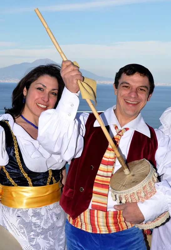 A smiling couple in costume, he plays the scetavajasse, with the bay and Vesuvius behind