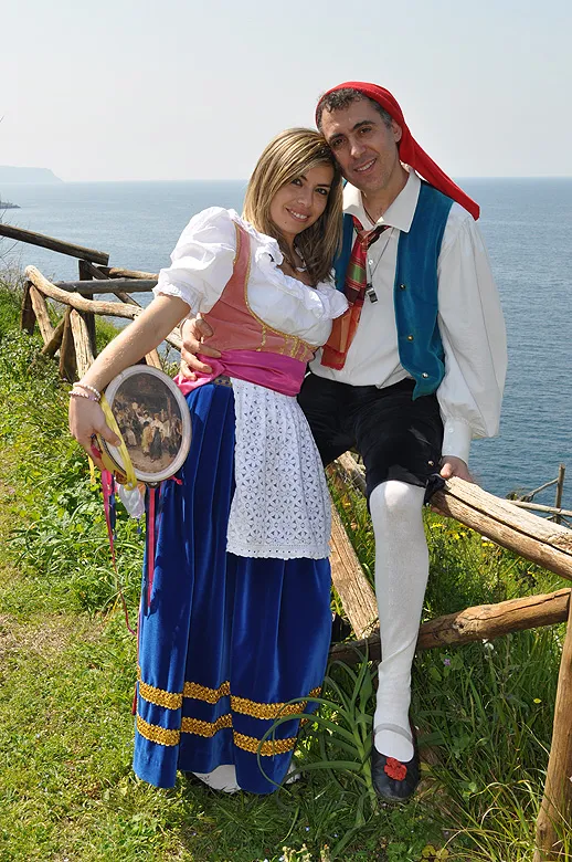 A couple in traditional costume embracing on a wooden fence high above the sea