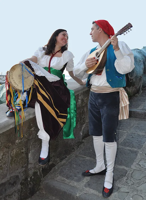 A dancer plays the mandolino for his partner, who sits on the low wall with her tambourine