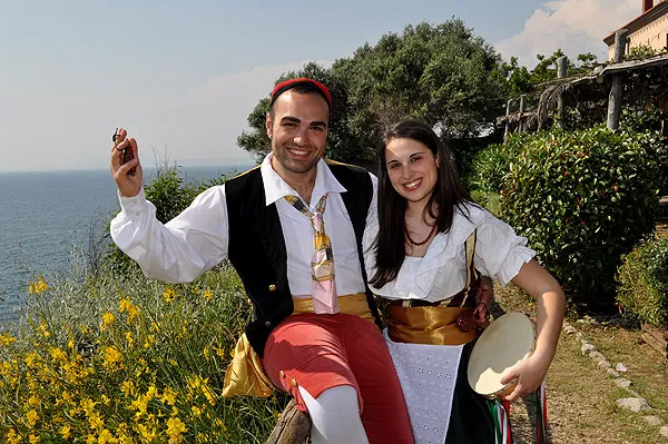 A couple in costume among flowering broom above the sea, he with castanets, she with a tambourine