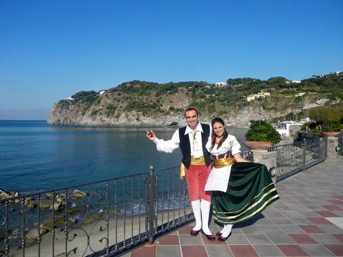 A couple in costume on a seaside terrace with a green headland behind them