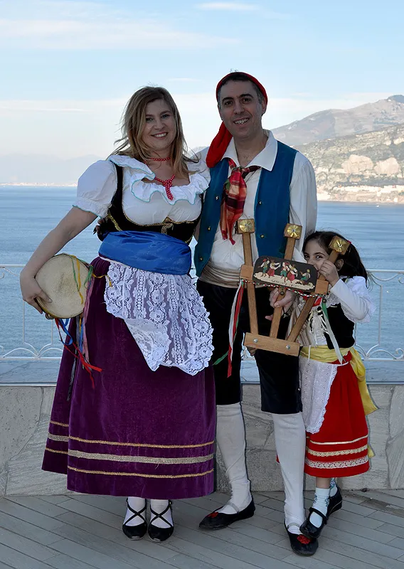 A couple and their little girl in traditional costume on a terrace above the bay, with tambourine and triccheballacche