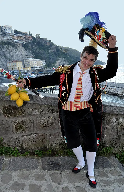 The Pazzariello lifting his large plumed hat above the harbour, lemons and staff in hand