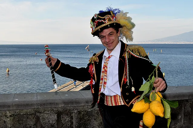The Pazzariello in his plumed hat holding a lemon branch in front of the Gulf of Sorrento