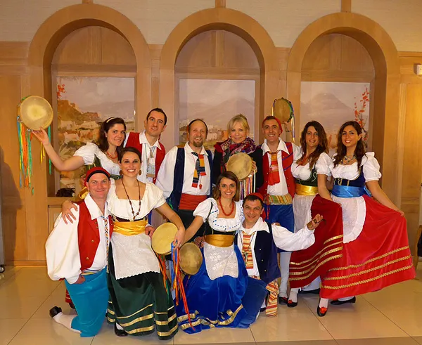 The costumed group posing with tambourines in a hall with painted arches