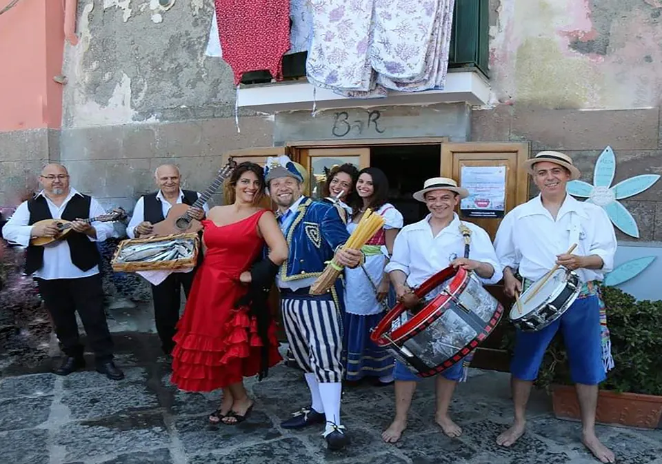 Musicians with mandolino, guitar and drums alongside costumed dancers in a village alley