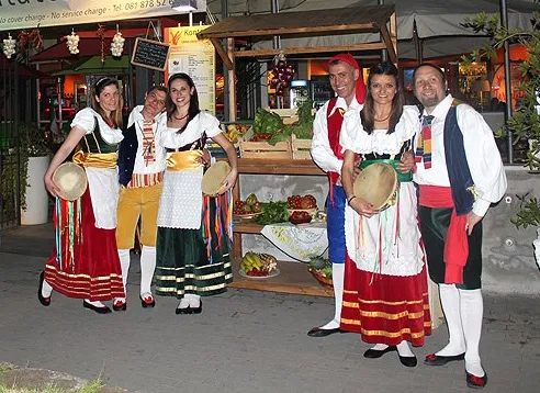 Ballerini in costume accanto a un banco di frutta in un ristorante