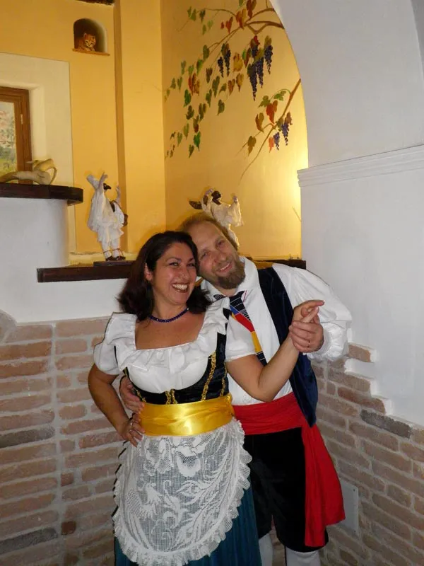 A couple in costume smiling arm in arm in a warmly lit restaurant room