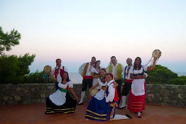 The costumed group on a terrace at dusk, the sea on the horizon