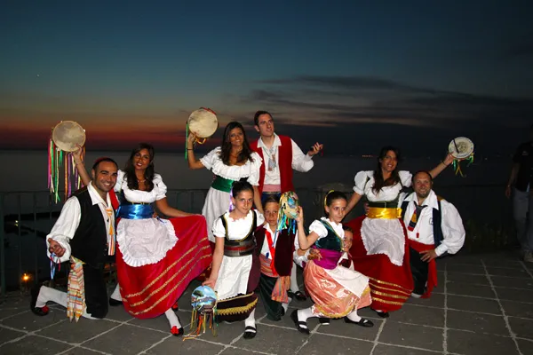 The group raising tambourines on a sea-view terrace at sunset during a hotel evening