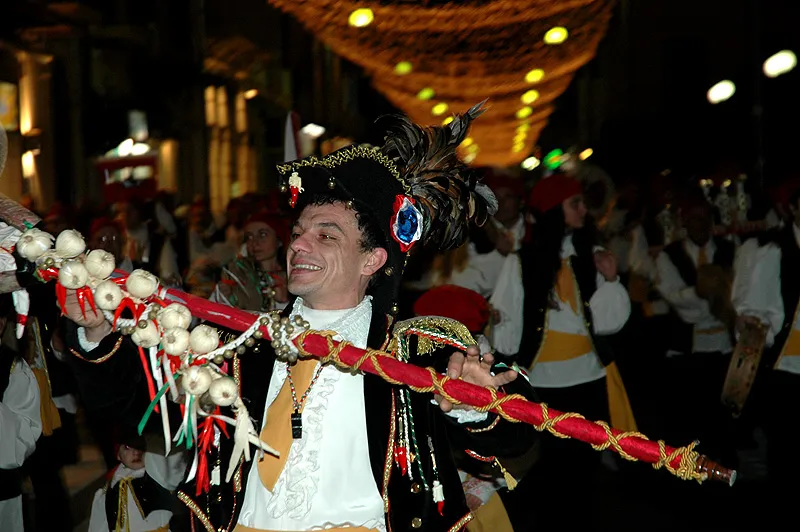 The Pazzariello waving his decorated staff beneath the lights of a village festival