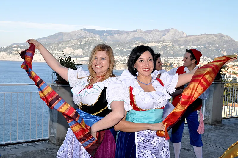 Ballerine sorridenti sventolano foulard a quadri colorati su una terrazza affacciata sul golfo di Sorrento