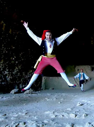 A dancer in traditional costume leaping with arms and legs outstretched inside a cave