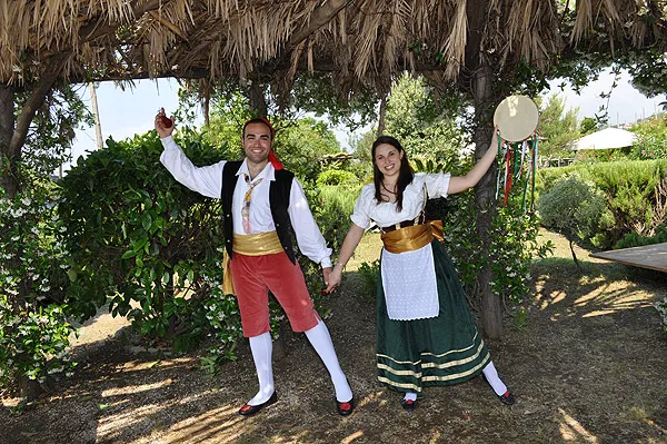 A couple dancing beneath a thatched pergola, her tambourine raised