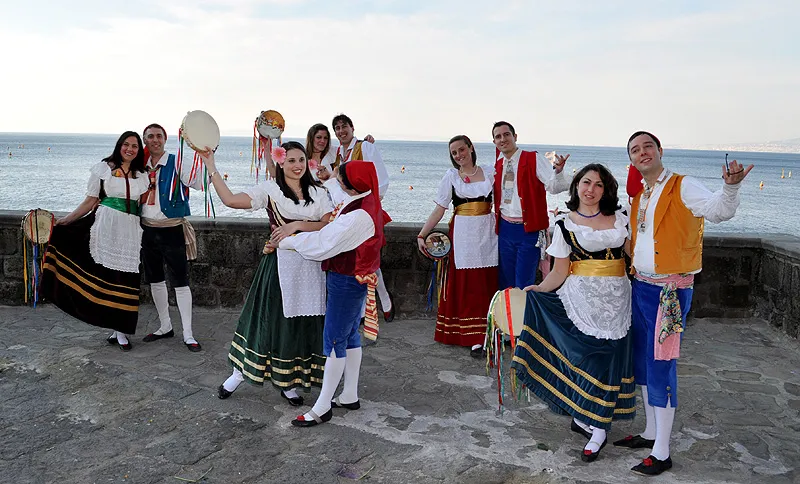 Couples with tambourines dancing on the seafront with the sea behind them