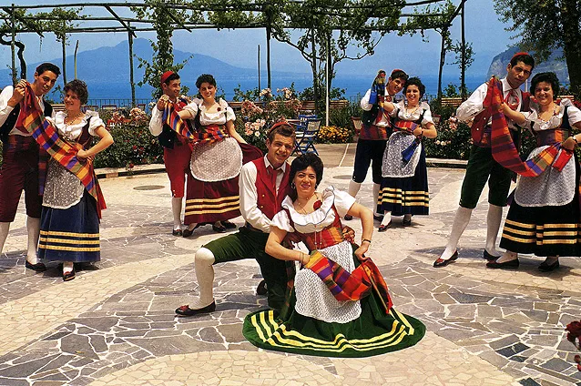 Coppie danzano la tarantella sorrentina sotto un pergolato, su un pavimento a mosaico con vista mare