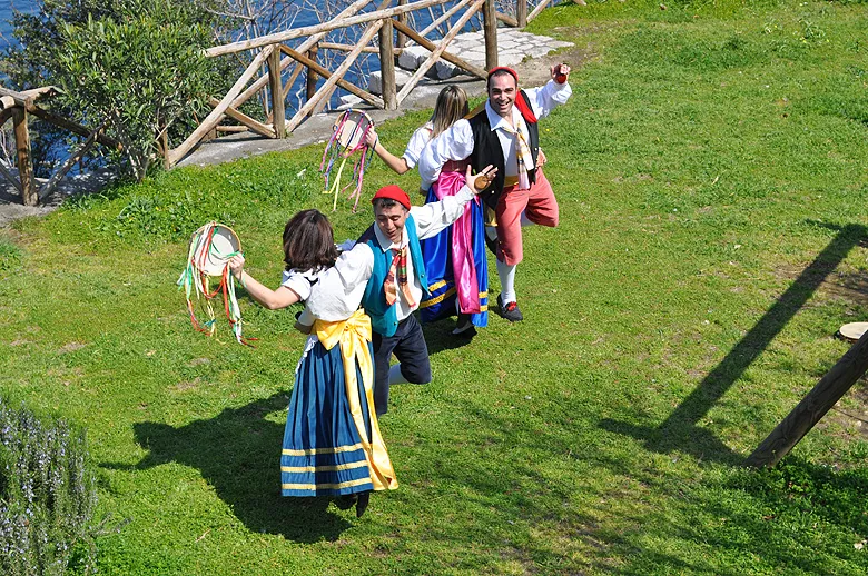 Couples dance the tarantella sorrentina with tambourines on a green lawn by a wooden fence