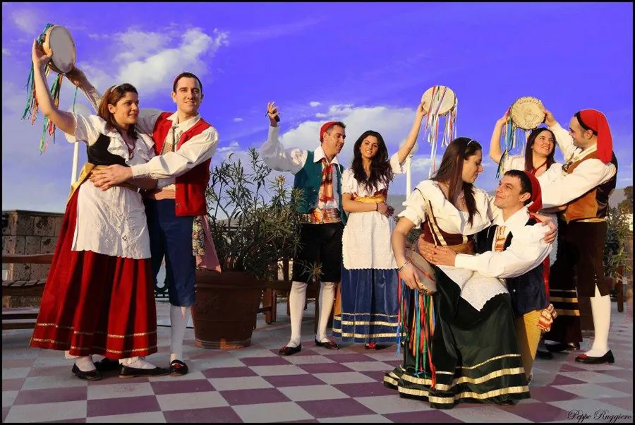 Couples of dancers in costume raising tambourines on an outdoor checkered floor
