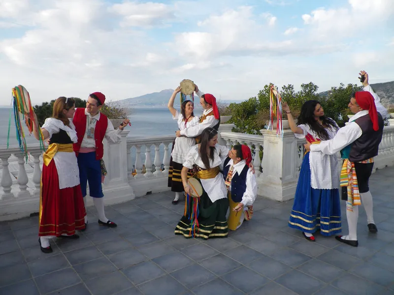 Coppie di ballerini danzano la tarantella sorrentina su una terrazza con balaustra affacciata sul golfo di Sorrento