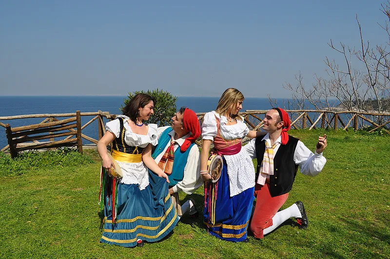 Kneeling dancers court their partners on a lawn above the sea, a classic tarantella gesture