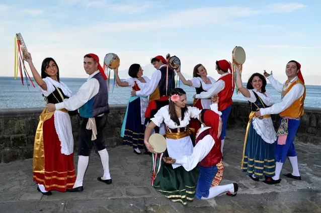 The group dancing with raised tambourines on the seafront, the bay in the background